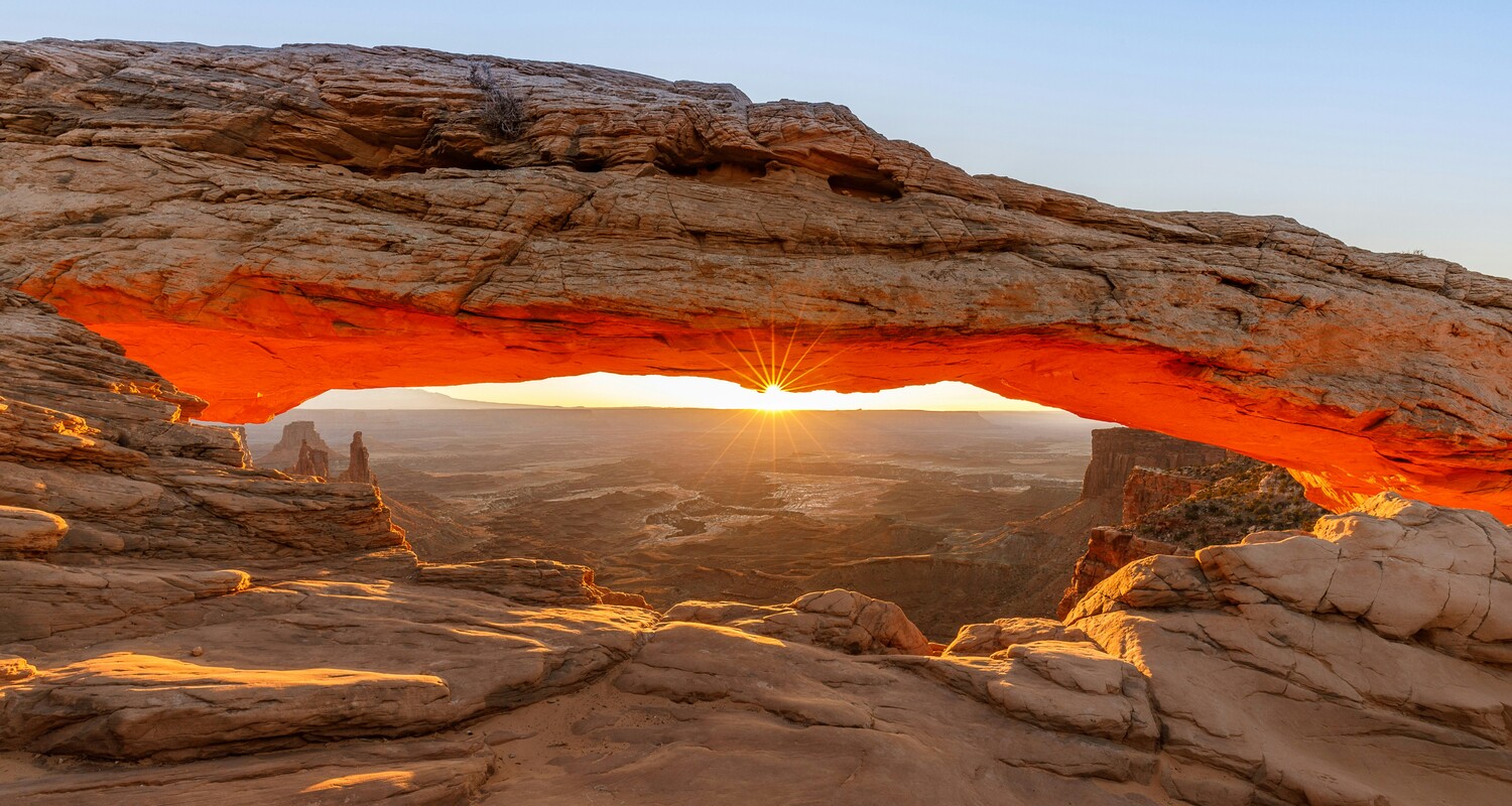 a sun shining through a rock arch