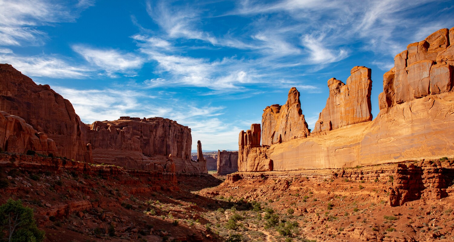 a rocky canyon with blue sky with Arches National Park in the background